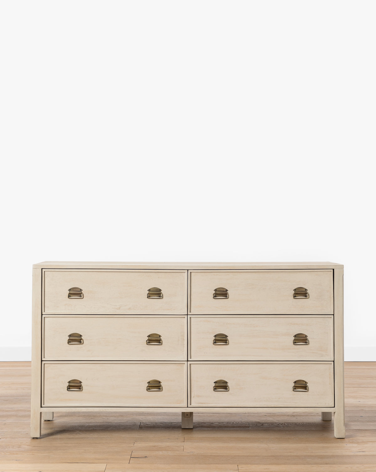 The Mackenna White Oak Dresser, featuring six drawers and elegant brass pulls, stands on a hardwood floor against a plain white wall, by McGee & Co.