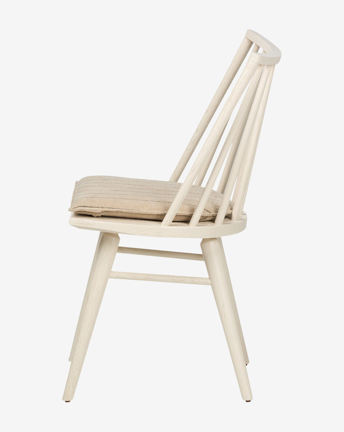 Side view of the Madison Dining Chair with angled legs, a slatted backrest, and a beige cushioned seat. Painted in light off-white, this minimalist chair brings modern comfort to any dining space, by McGee & Co.