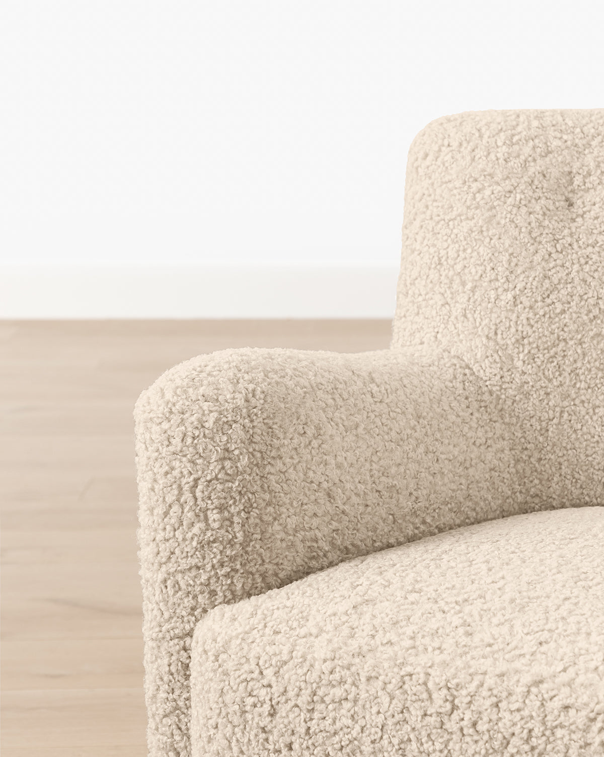 Close-up of the left armrest and seat of a beige, textured Magda Lounge Chair (Ready to Ship) in boucle upholstery, shown on a light wood floor with a white wall background, by McGee & Co.