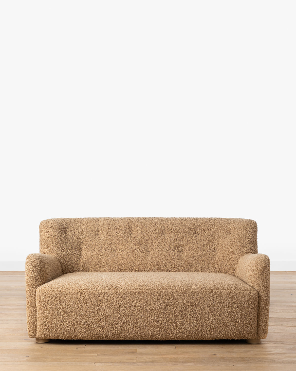 The Magda Settee 65.25 (Ready to Ship) features plush beige boucle upholstery and a sleek white oak frame, sitting on a wooden floor against a plain white wall, by McGee & Co.