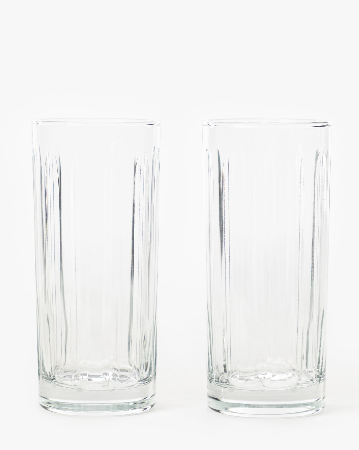 A set of two empty, clear Marick Highball Glasses with classic silhouettes stands side by side on a plain white background by McGee & Co.