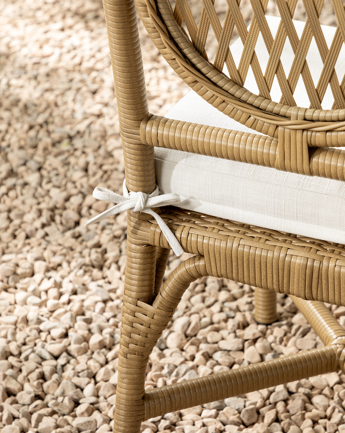 Close-up of a Marisol Indoor/Outdoor Dining Chair (Set of 2), featuring handwoven wicker and a white cushion tied to the seat, placed on light-colored pebbles by McGee & Co.