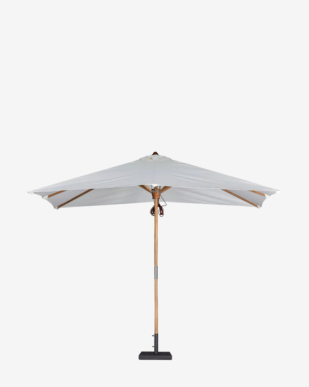 The Marques Outdoor Rectangular Umbrella, featuring a large white canopy and teak pole, stands on a textured gravel surface against a light beige stucco wall, casting soft shadows in this minimalist outdoor space, by McGee & Co.