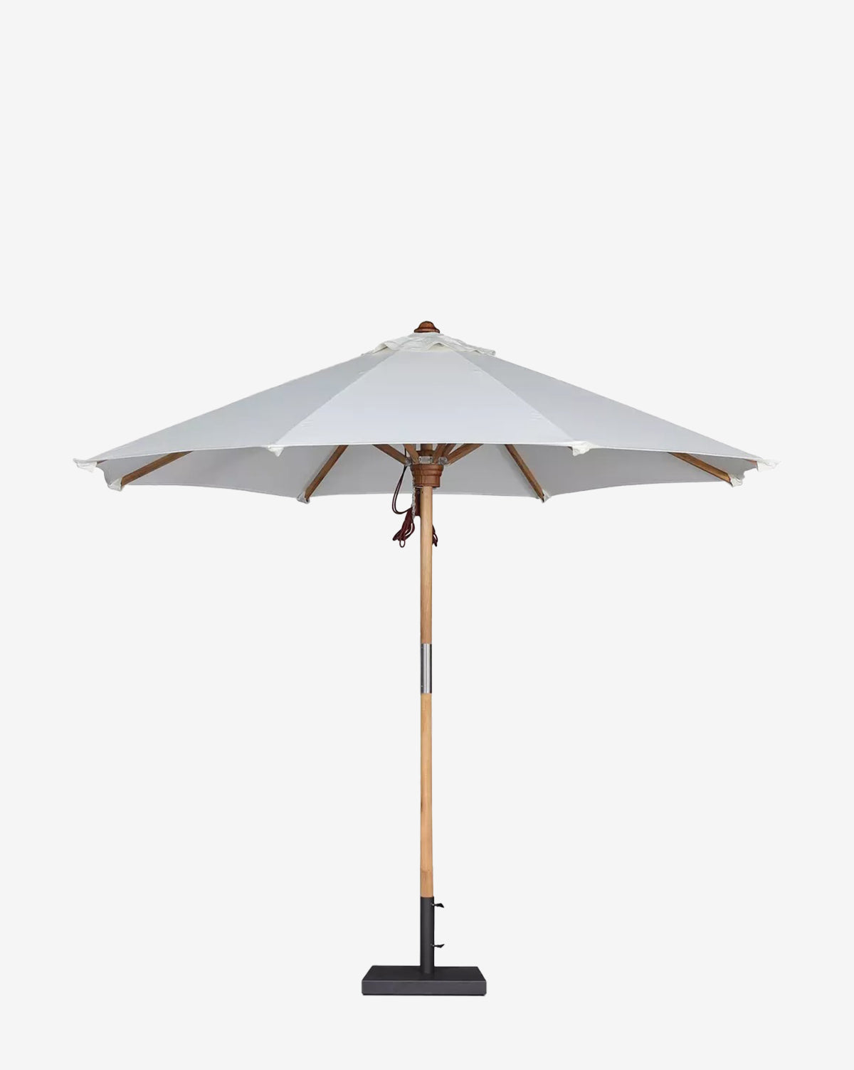 The Marques Outdoor Round Umbrella features a weather-resistant acrylic white canopy and sturdy teak pole, standing on textured gravel against a light beige stucco wall with soft background shadows, by McGee & Co.