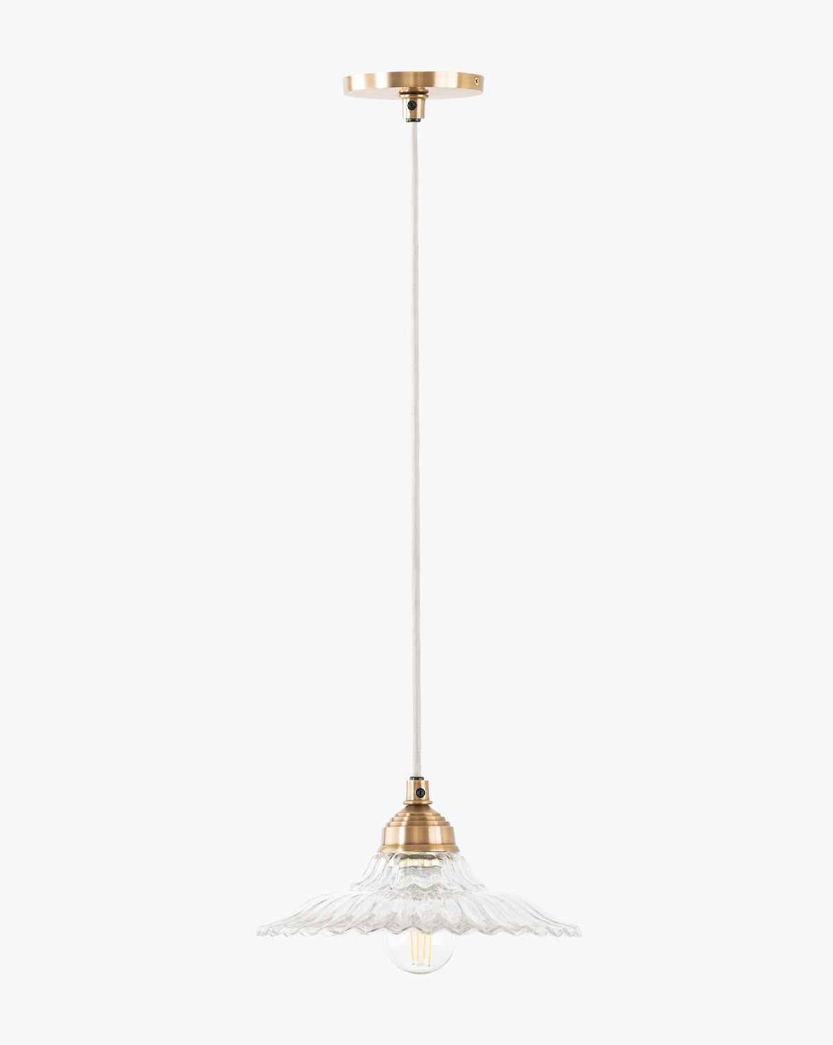 The McGee & Co. x Loeffler Randall Maude Glass Pendant features brass hardware, a white cord, and a clear scalloped glass shade that beautifully displays an exposed bulb, by McGee & Co.