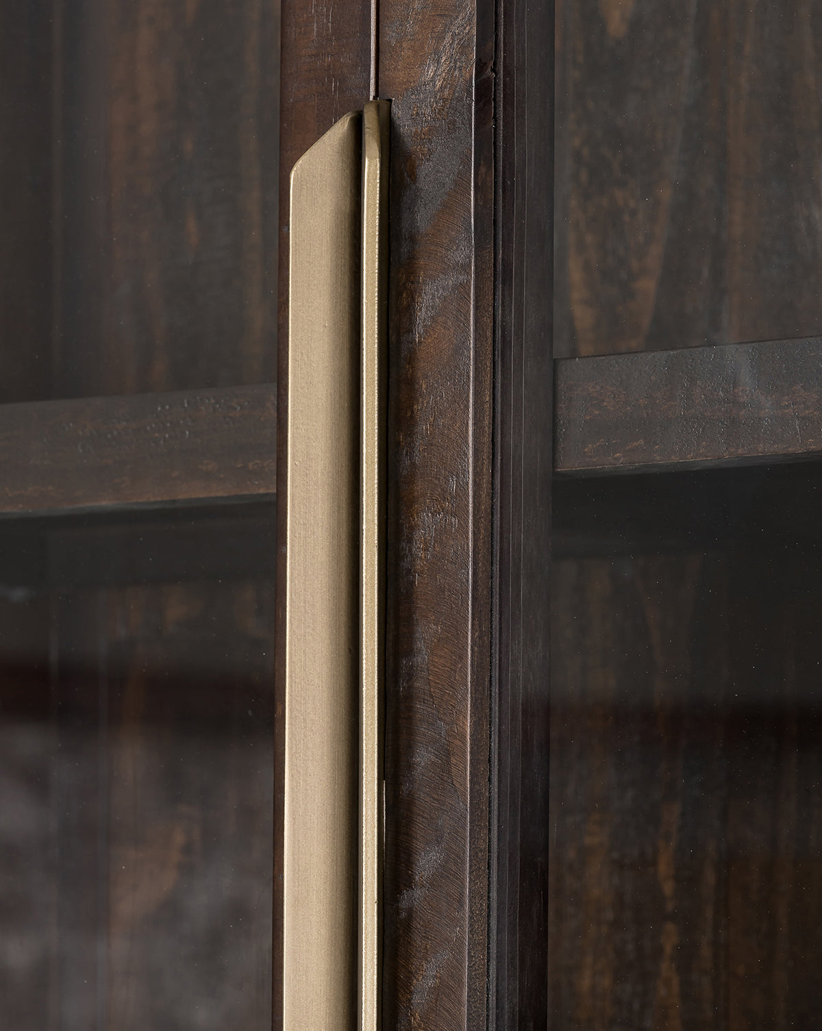 Close-up of the Maverick Cabinet, crafted from reclaimed pine with glass paneled doors. A vertical metallic gold handle accents the dark wood, showing off interior shelves and natural wood grain through the glass, by McGee & Co.