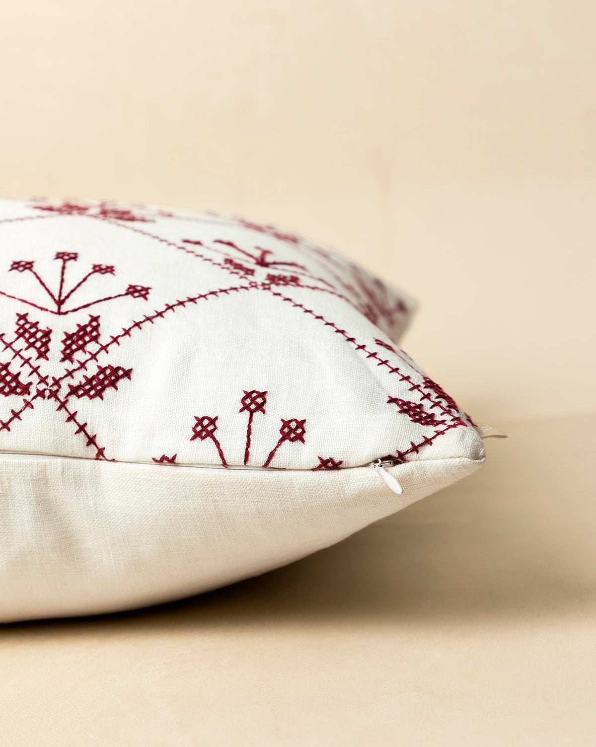 A close-up of the McCallister Pillow Cover showcases maroon embroidered geometric and floral designs on white fabric, set on a beige background. A subtle zipper adds elegance—perfect for holiday home decor, by McGee & Co.