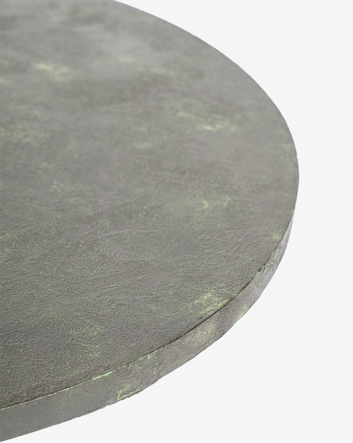 Close-up of the edge of a round, textured gray-green zinc tabletop from the Mellie Outdoor Table, set against a plain white background by McGee & Co.