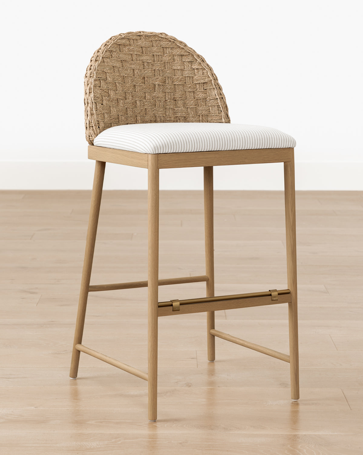 The Molly Stool, made from solid oak with a woven rattan curved backrest and cushioned light striped fabric seat, is placed on a light wood floor against a plain white wall by McGee & Co.