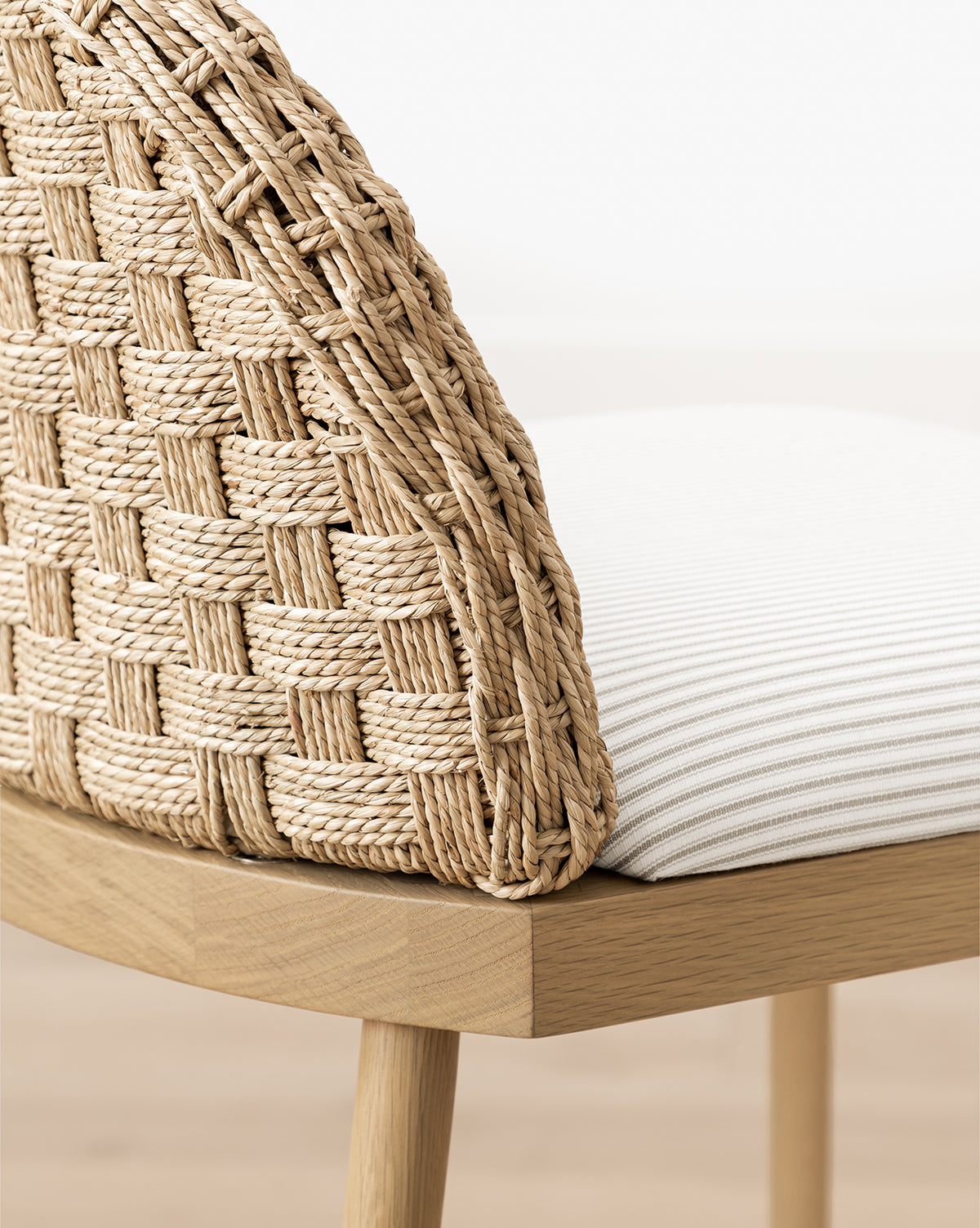 Close-up of the Molly Stool featuring a woven rattan backrest in a basket-weave pattern, solid oak frame, and a white upholstered seat cushion with subtle vertical stripes, by McGee & Co.