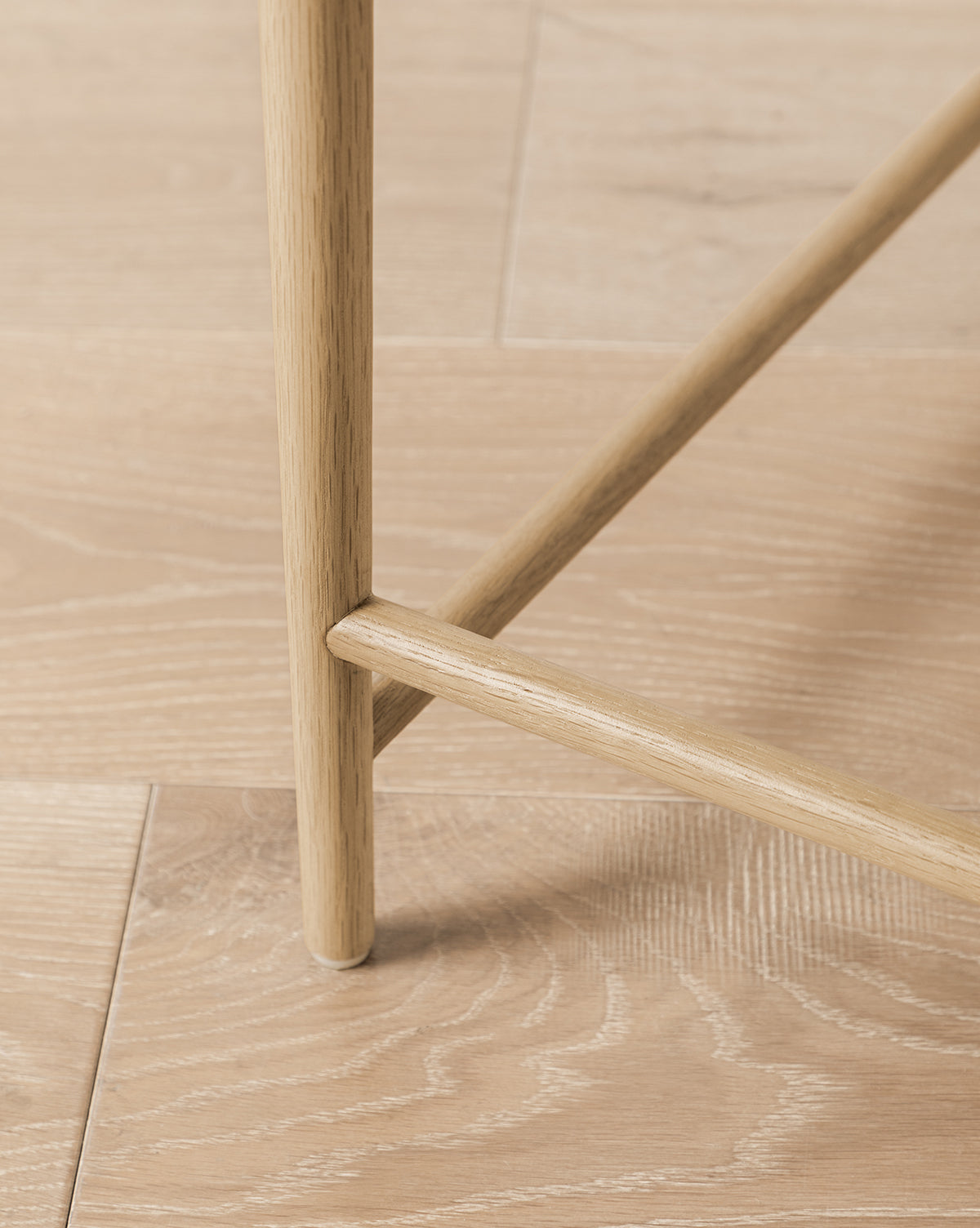 Close-up of Molly Dining Chairs solid oak legs intersecting on a light wood floor, emphasizing the rich wood grain and texture of both the chair and floorboards, by McGee & Co.