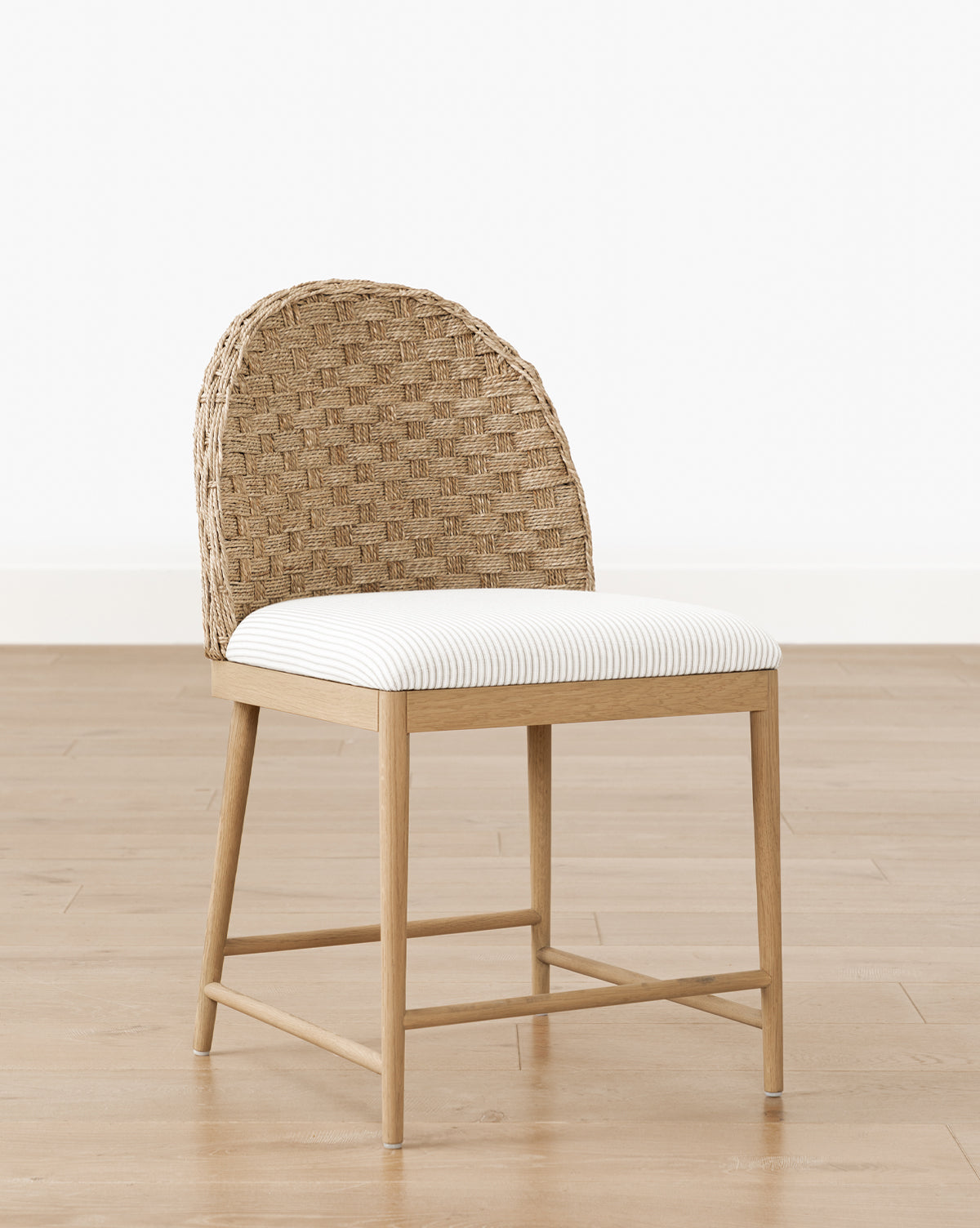 The Molly Dining Chair, crafted from solid oak with a woven curved back and white cushioned seat, is placed on a light wood floor against a plain white wall, by McGee & Co.
