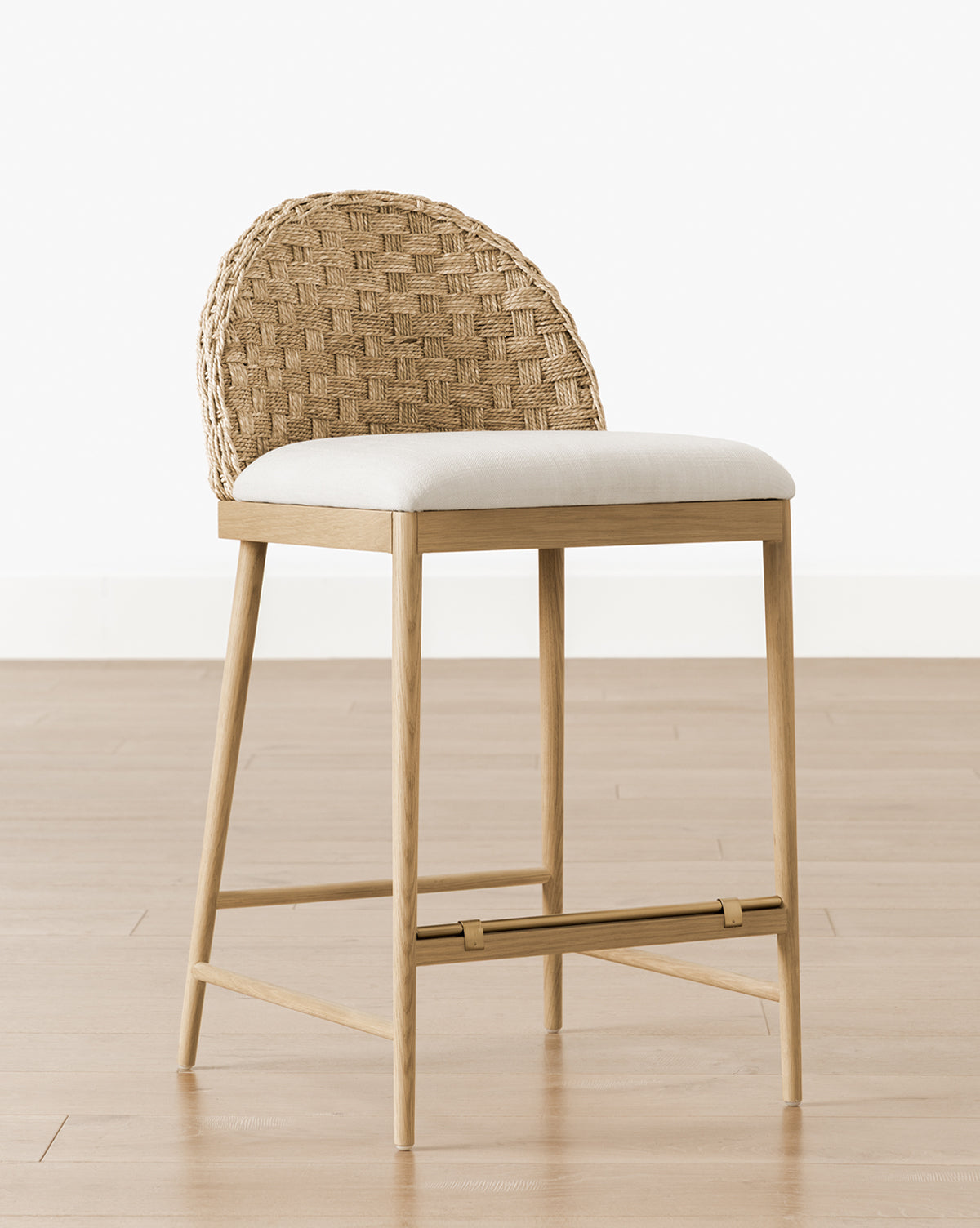The Molly Stool features a woven rattan rounded backrest, a cushioned light beige seat, and solid oak construction, shown on a light wooden floor against a plain white wall by McGee & Co.