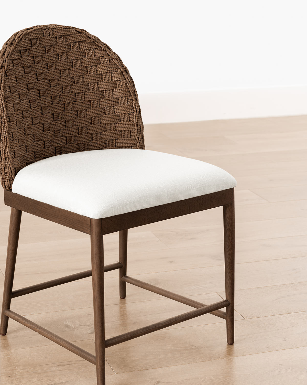 The Molly Dining Chair showcases a woven curved backrest and white cushioned seat, with a modern design crafted from solid oak—ideal for light wood floors and white walls, by McGee & Co.
