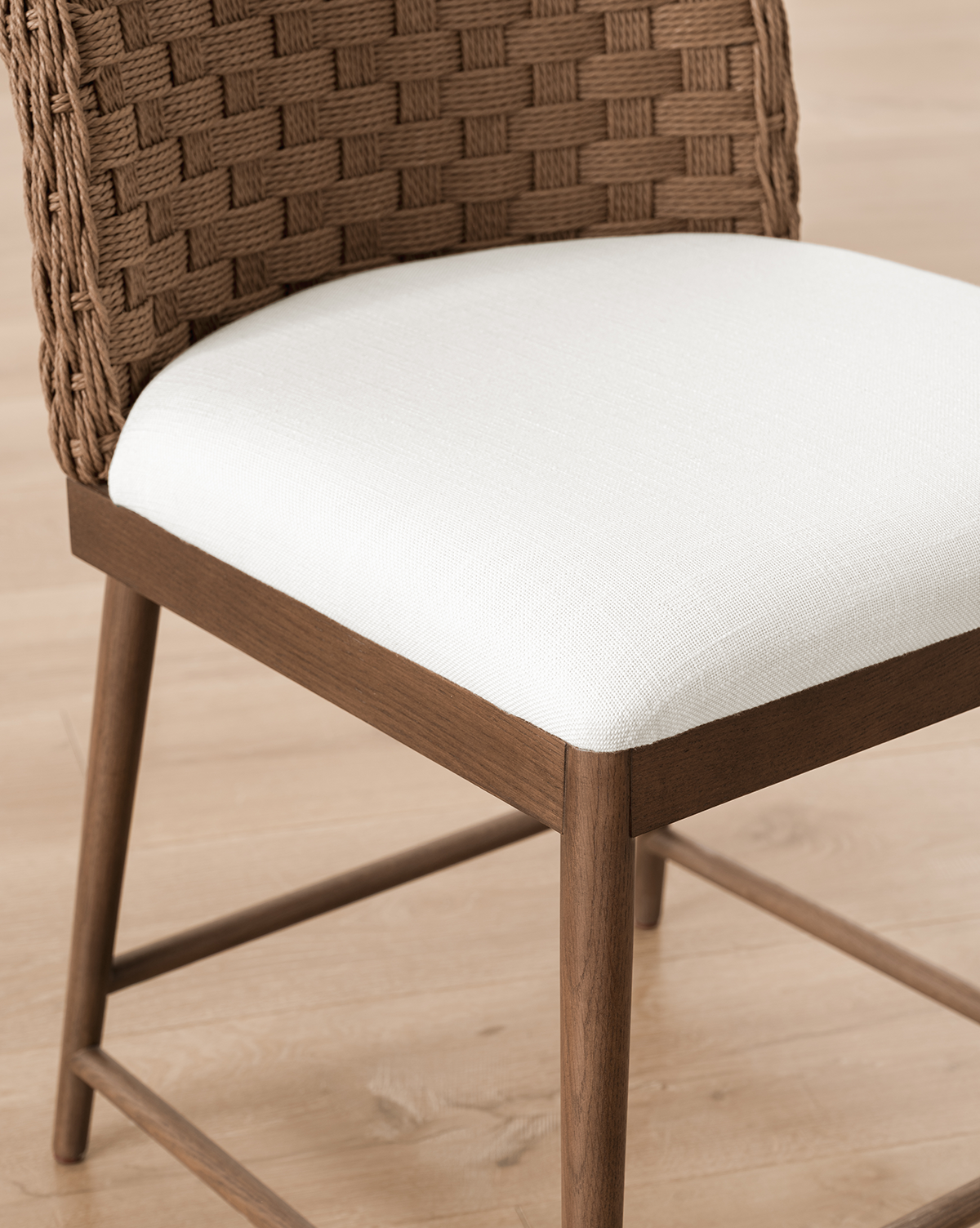 The Molly Dining Chair features a woven brown backrest, white cushioned seat, and solid oak legs, shown here on a light wood floor, by McGee & Co.