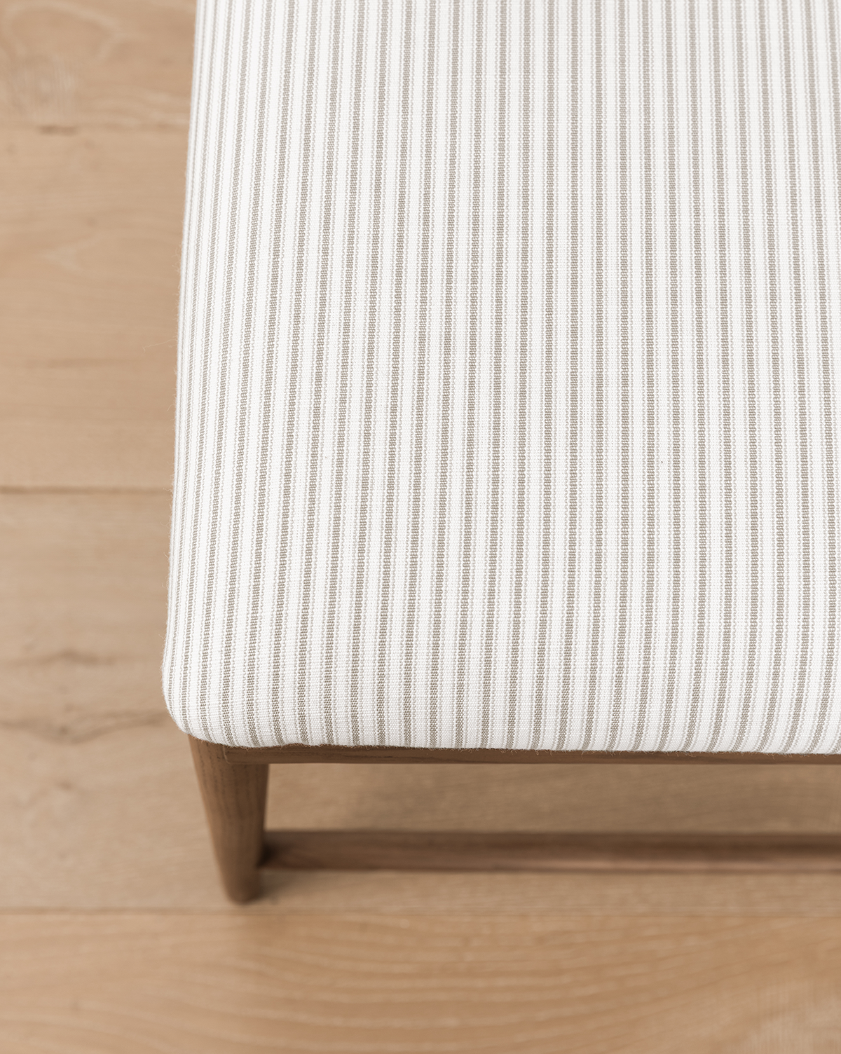 The Molly Stool features a seat with white and light grey vertical stripes and solid oak legs, shown here on a light wood floor, by McGee & Co.