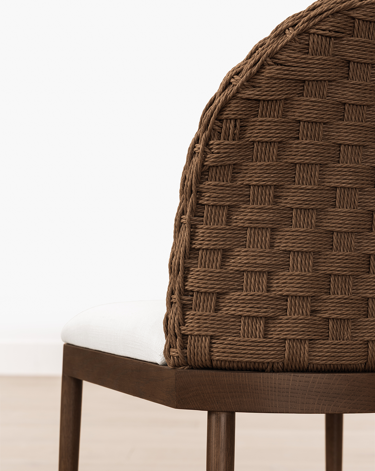 A close-up of the Molly Stool, featuring a solid oak frame, brown woven backrest, and white cushioned seat, set against a plain white wall and light wood floor, by McGee & Co.