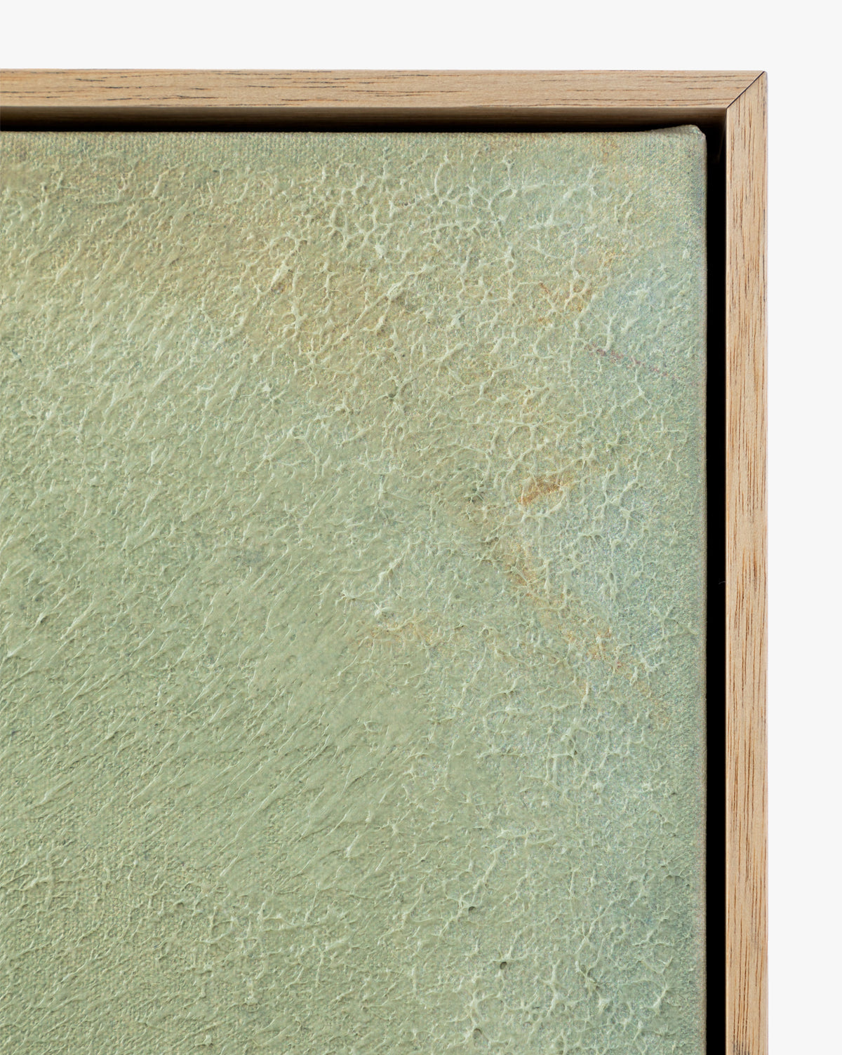 Close-up of the corner of Moss, a textured, light green gallery-wrapped canvas painting in a natural wood frame, highlighting cracks and visible brushstrokes on its painted surface.