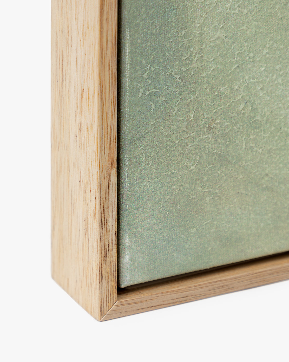 Close-up of the corner of a natural wood frame holding Moss, a textured green artwork, set against a white background.