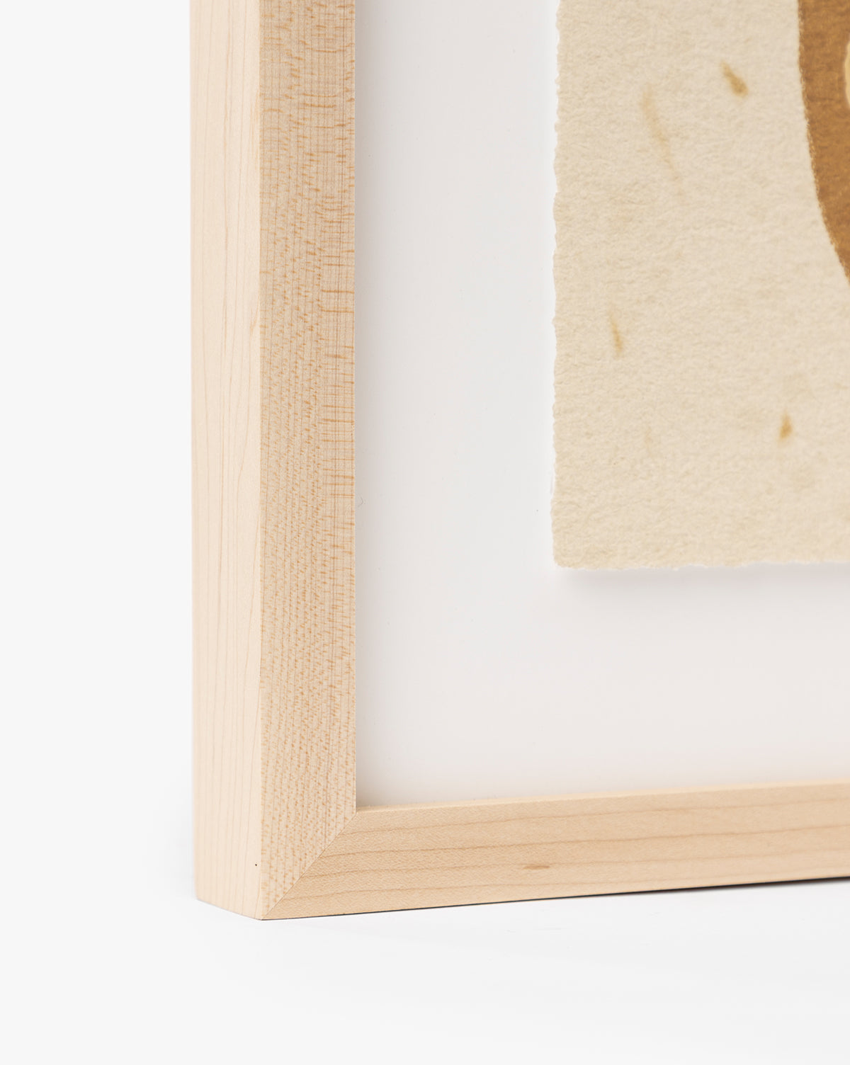 Close-up of the bottom left corner of a maple frame for Moth IV By Coup dEsprit, showing part of its textured, off-white abstract art. The image highlights the frame’s clean lines and natural wood grain, by McGee & Co.