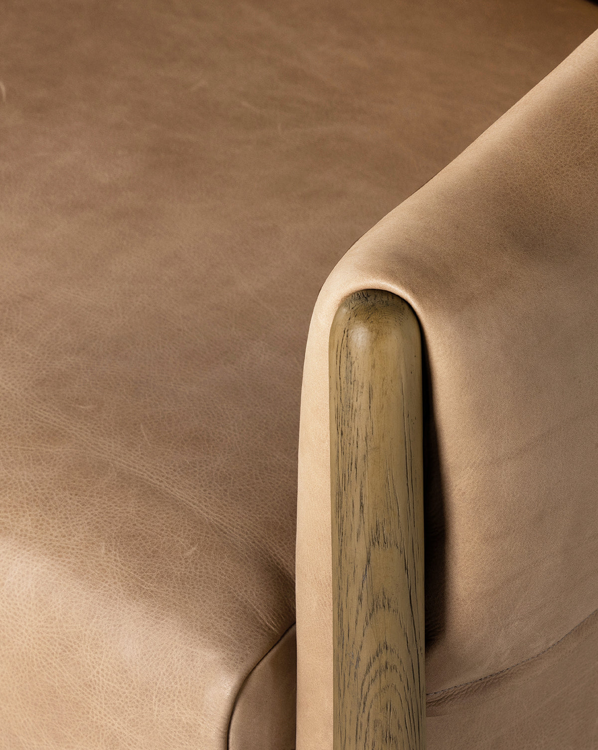 Close-up of the Nadine Lounge Chair, showcasing its tan leather upholstery, smooth seat cushion, rounded wooden armrest with visible grain, and a plush gray cushion by McGee & Co.