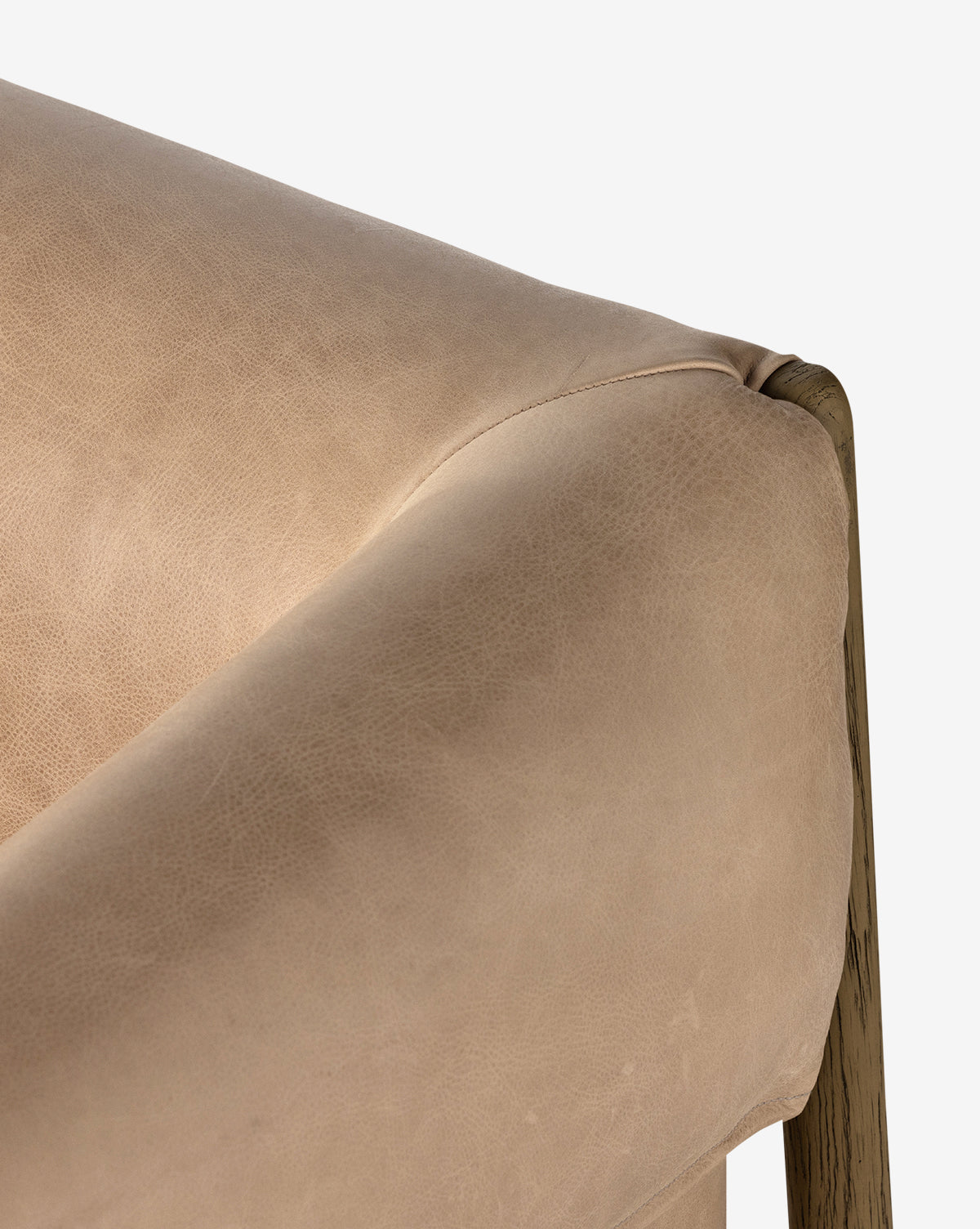 Close-up of the Nadine Lounge Chair’s corner, showcasing its beige leather upholstery and solid oak frame, with the smooth texture of the material highlighted against a white background, by McGee & Co.