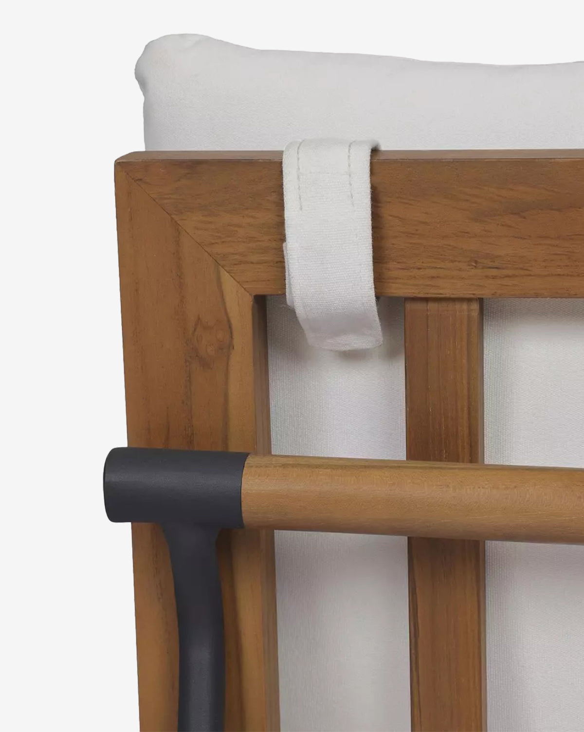 Close-up of the Neal Outdoor Dining Chair, showcasing its teak frame with vertical slats, black metal support bar, and white performance fabric seat cushion secured at the top with a fabric loop by McGee & Co.