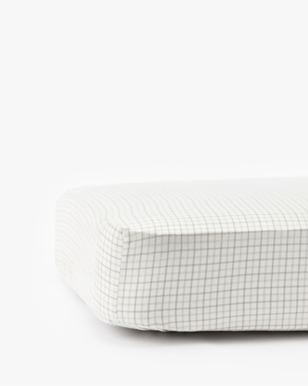 A close-up of the Nell Blue Crib Sheet shows its light gray and white plaid fabric cover, perfect for childrens bedding, displayed against a plain white background by McGee & Co.