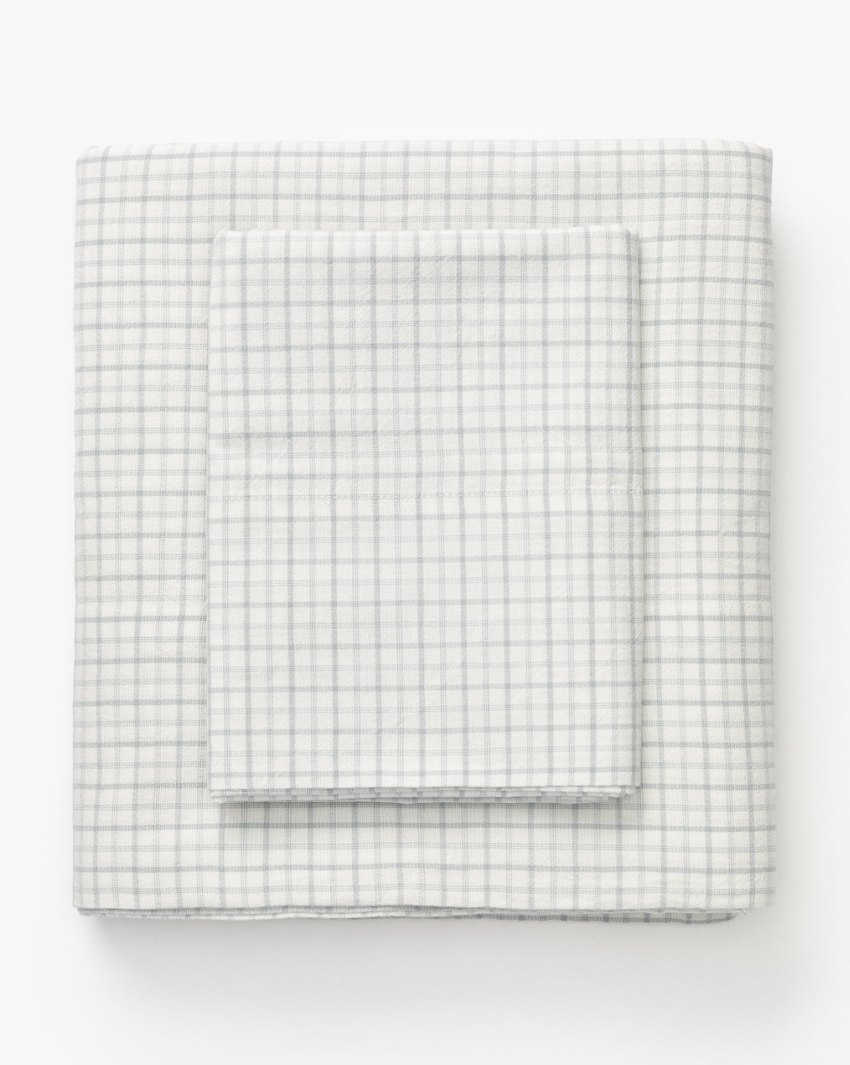 The Nell Blue Twin Kids Sheet Set includes three neatly folded white cotton sheets with a subtle light gray checkered pattern, ideal for plaid bedding, shown against a plain white background by McGee & Co.