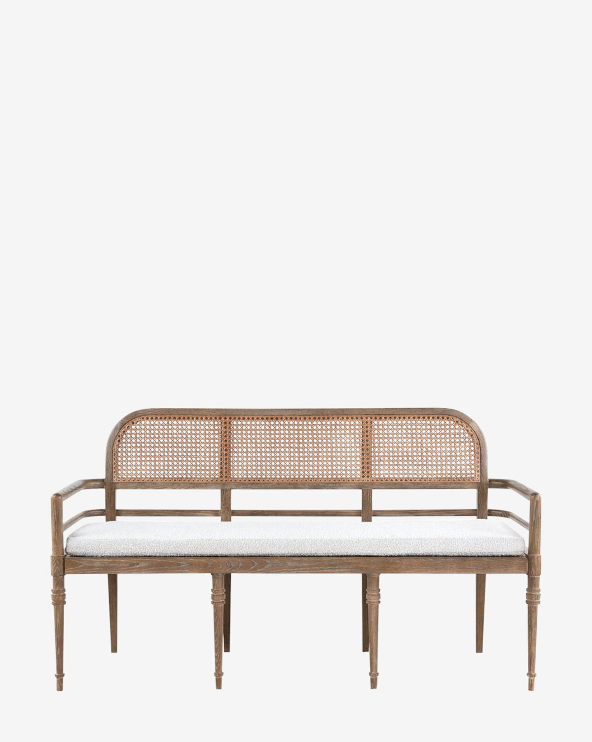 The Nestor Bench showcases a woven rattan backrest and armrests, carved oak frame, and a white boucle cushion. Its natural wood finish contrasts beautifully with the plain white background, by McGee & Co.