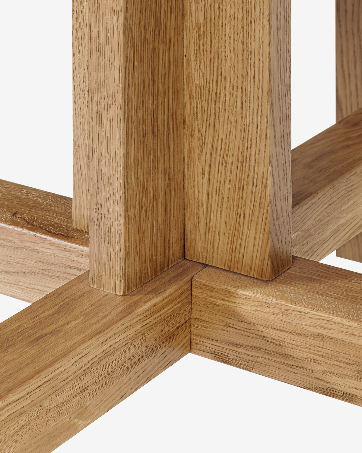 Close-up of intersecting wooden beams with a honey finish on the Newbold Dining Table, forming a sturdy joint. The visible wood grain and texture highlight its modern design elements by McGee & Co.