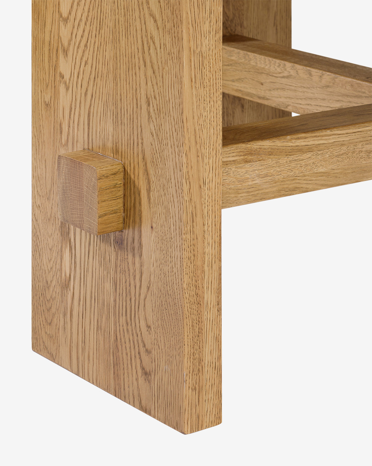 Close-up of a Newbold Dining Table leg with a visible joint and rectangular peg, showcasing natural oak grain. The light honey finish accentuates the texture, highlighting its modern design by McGee & Co.