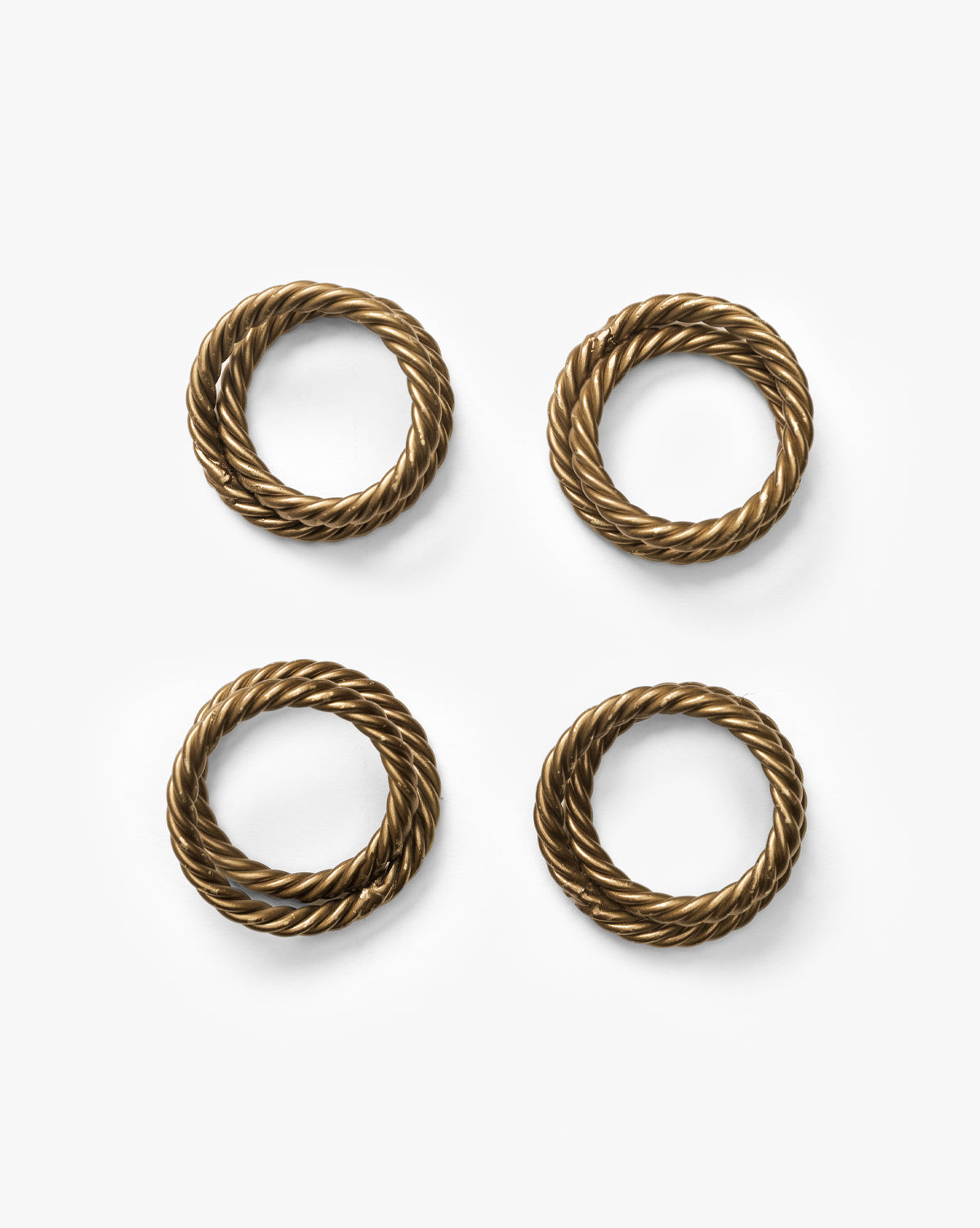 The Nichols Napkin Rings (Set of 4) feature round, twisted rope designs in antique brass, arranged on a white background—an ideal choice for an elegant table setting, by McGee & Co.