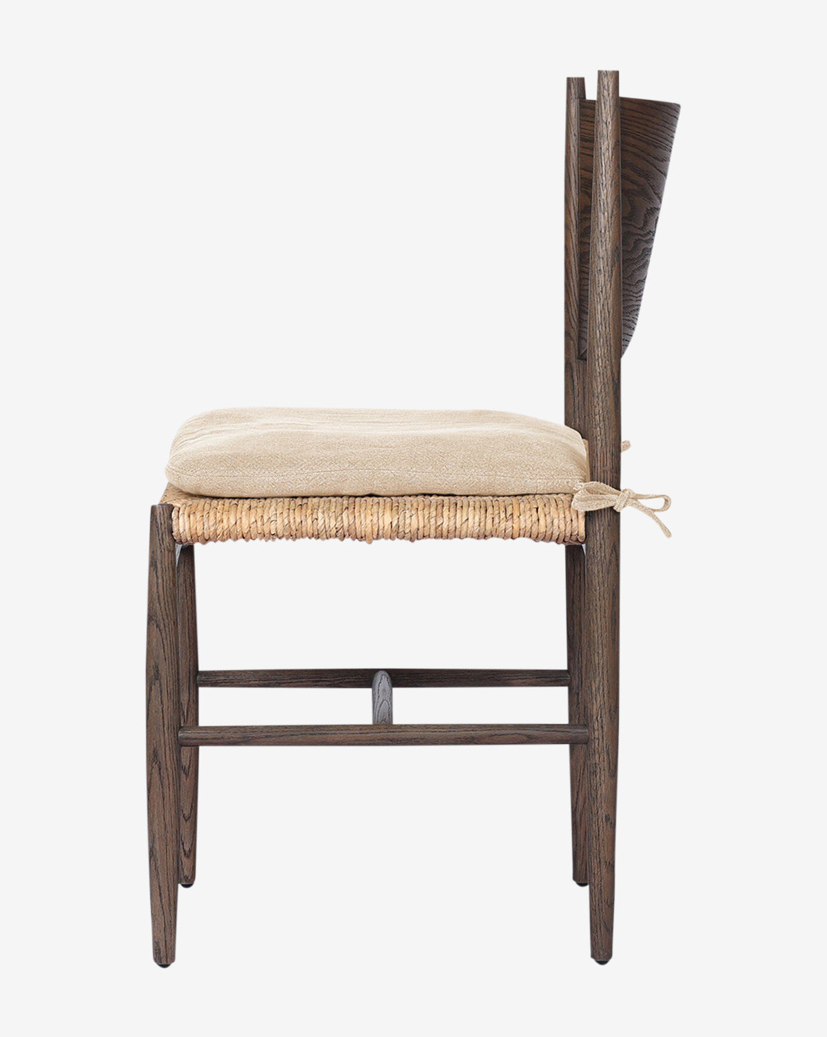 Side view of the Nixie Dining Chair: solid oak frame in dark finish, woven banana leaf seat, curved backrest, and a beige high-performance fabric cushion tied on, by McGee & Co. Shown against a plain white background.