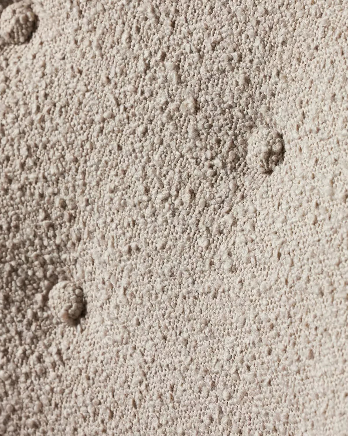 A close-up of the Olivette Slipper Chair’s textured beige upholstery, featuring small bumps and two larger, rounded indentations typical of its modern design, by McGee & Co.