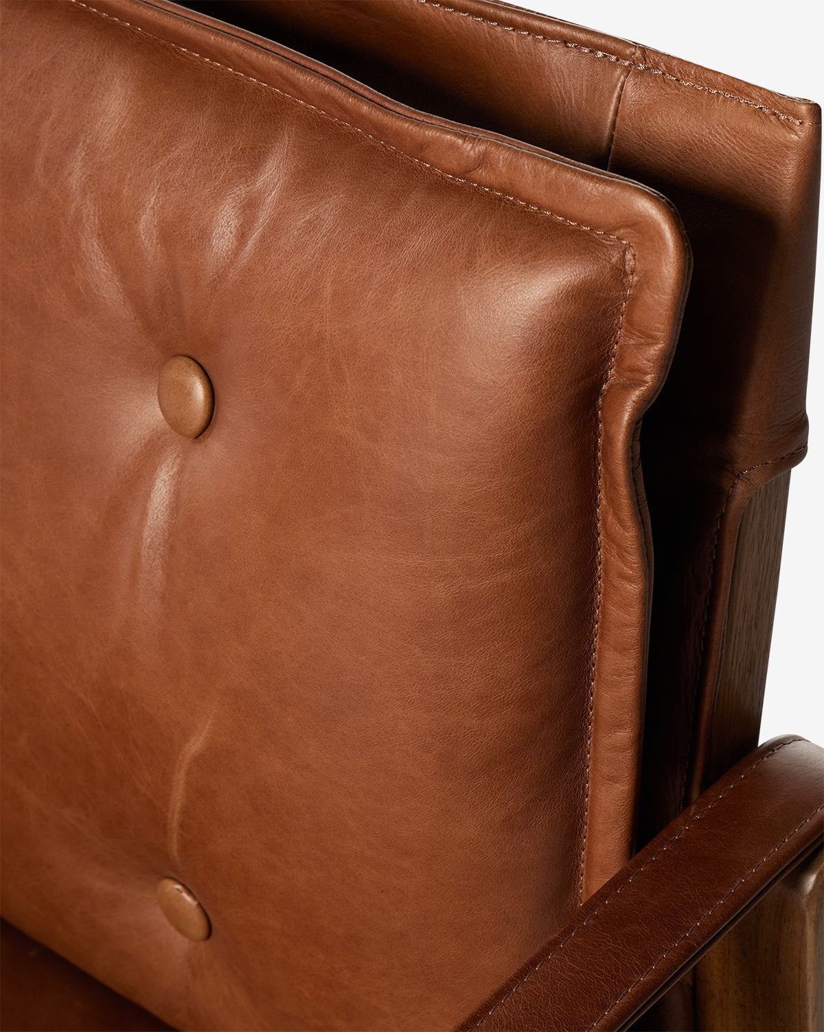 Close-up of the Pederson Dining Armchair, showcasing a smooth top grain leather seat with thick, button-tufted cushions and honey-finished wood armrests. Visible stitching and natural creases highlight its quality craftsmanship, by McGee & Co.