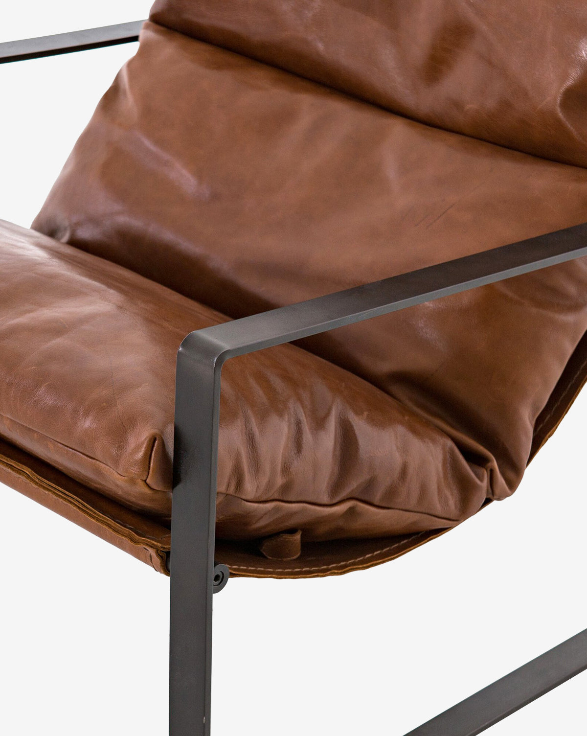 Close-up of the Peyton Leather Sling Chair, featuring a black metal frame and plush brown leather cushions. Its modern design emphasizes comfort with soft seat and backrest, complemented by clean, minimalist lines.