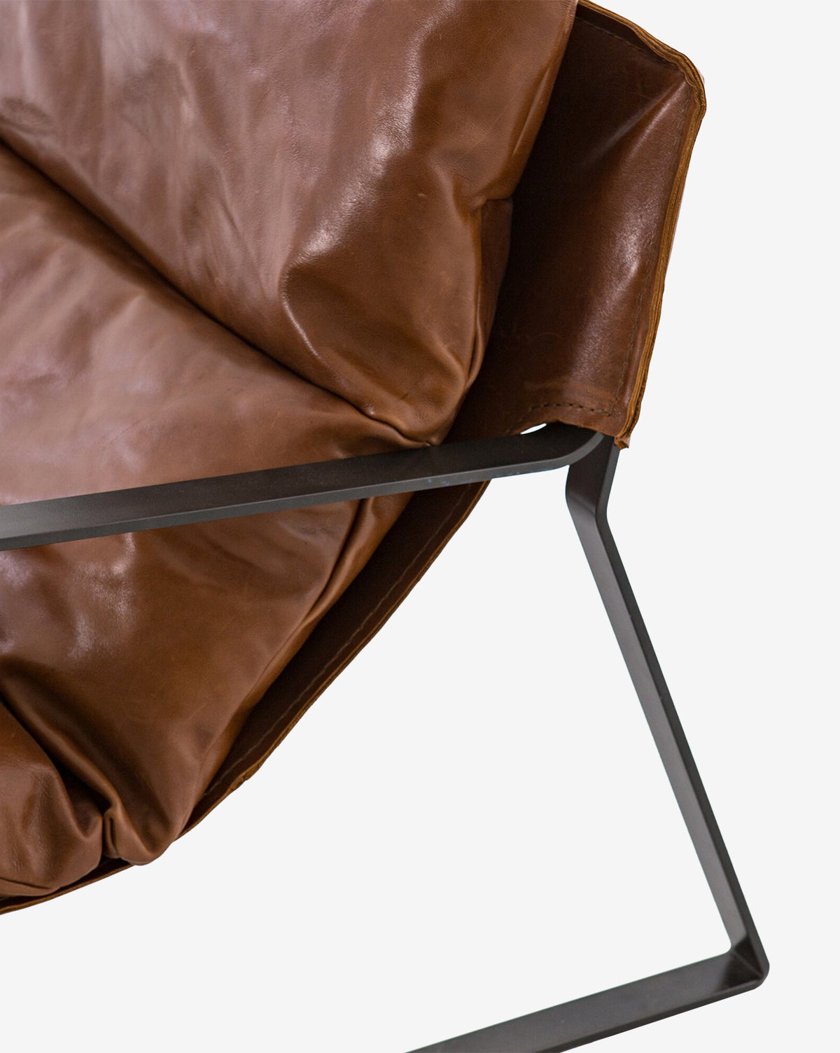 Close-up of the Peyton Leather Sling Chair, featuring brown leather cushions and a sleek black metal frame, set against a white background.