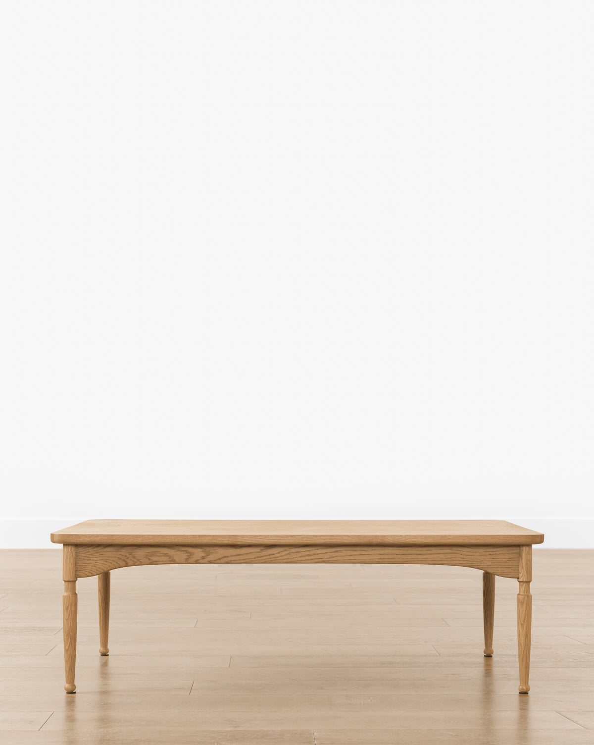 The Phipps Coffee Table, handcrafted with four tapered legs, stands on a light wood floor against a plain white wall, making it an ideal centerpiece for your living room, by McGee & Co.