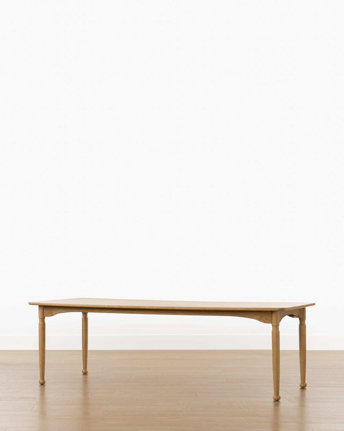 The Phipps Dining Table is a simple, handcrafted piece with four legs, shown on a light brown wooden floor against a plain white background by McGee & Co.