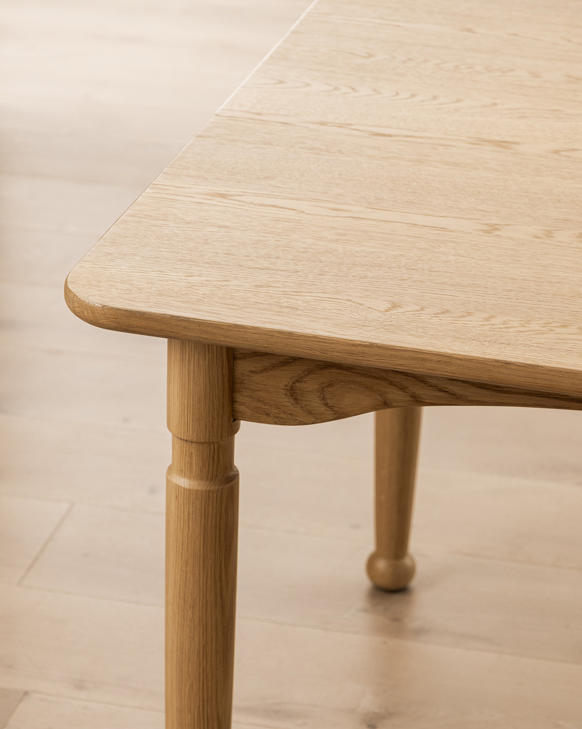 Close-up of the Phipps Dining Table’s corner, featuring rounded edges and turned legs, set on a matching light wood floor by McGee & Co.