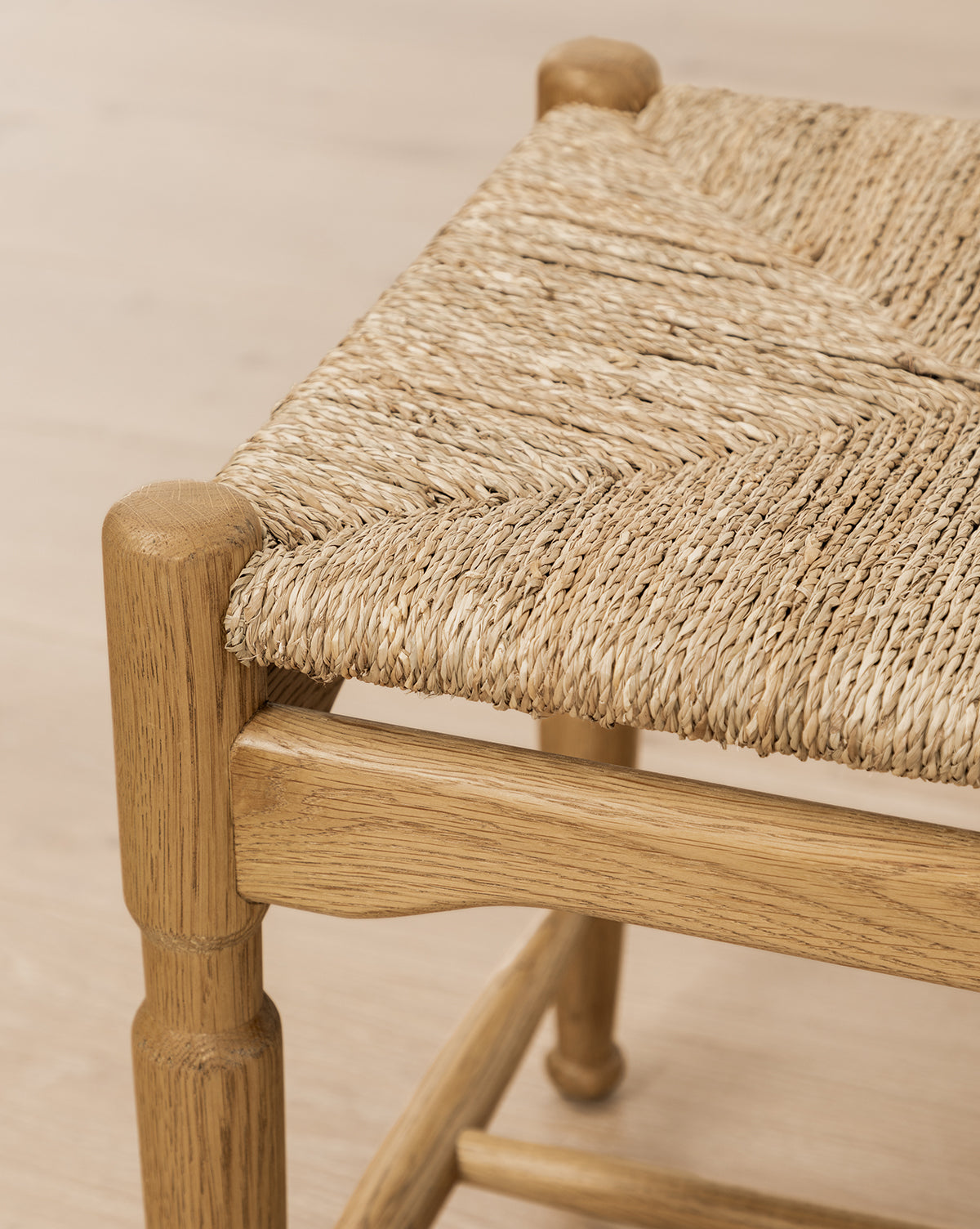 Close-up of the Phipps Woven Bench corner, showcasing its seagrass seats detailed weave and the smooth honey oak frame against a light wooden floor, by McGee & Co.