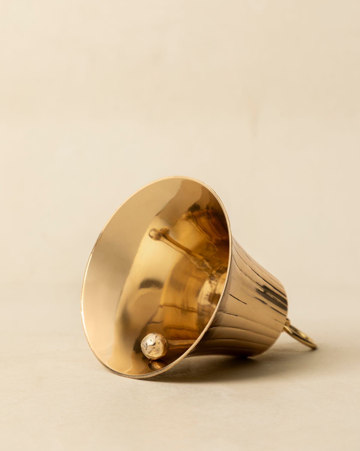 The Polished Brass Bell rests on a neutral surface, displaying its clapper and simple loop handle—ideal for adding vintage-inspired charm to your holiday décor, by McGee & Co.