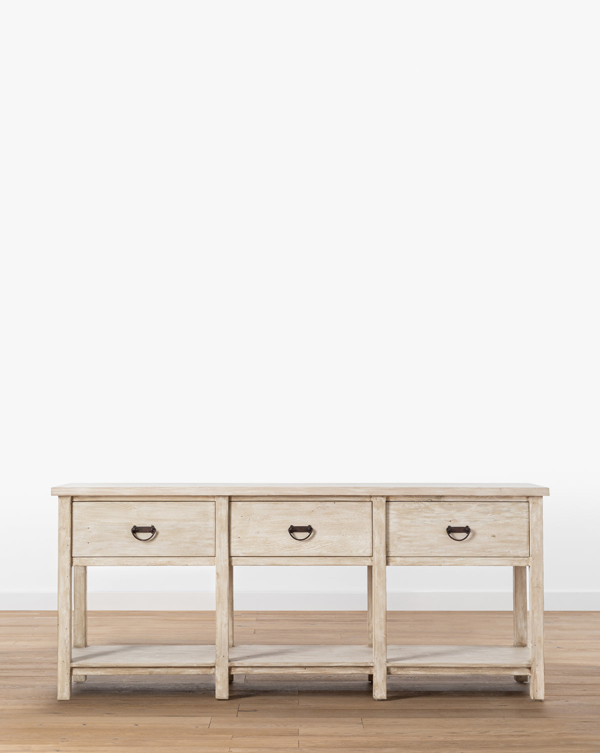 The Martha Sideboard, crafted from reclaimed Douglas Fir, features a light wood finish, three drawers with metal handles, a lower shelf, and stands on a wooden floor against a white background by McGee & Co.