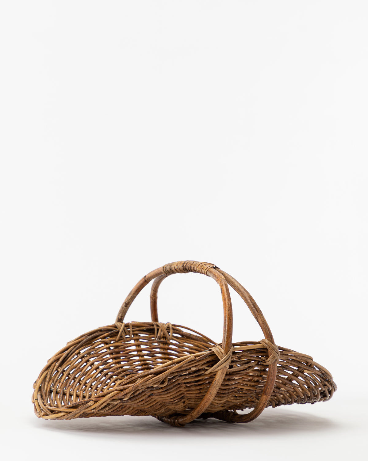 The Rattan Gardening Tray features a rounded shape and two curved handles, highlighting its natural texture and organic look against a plain white background.