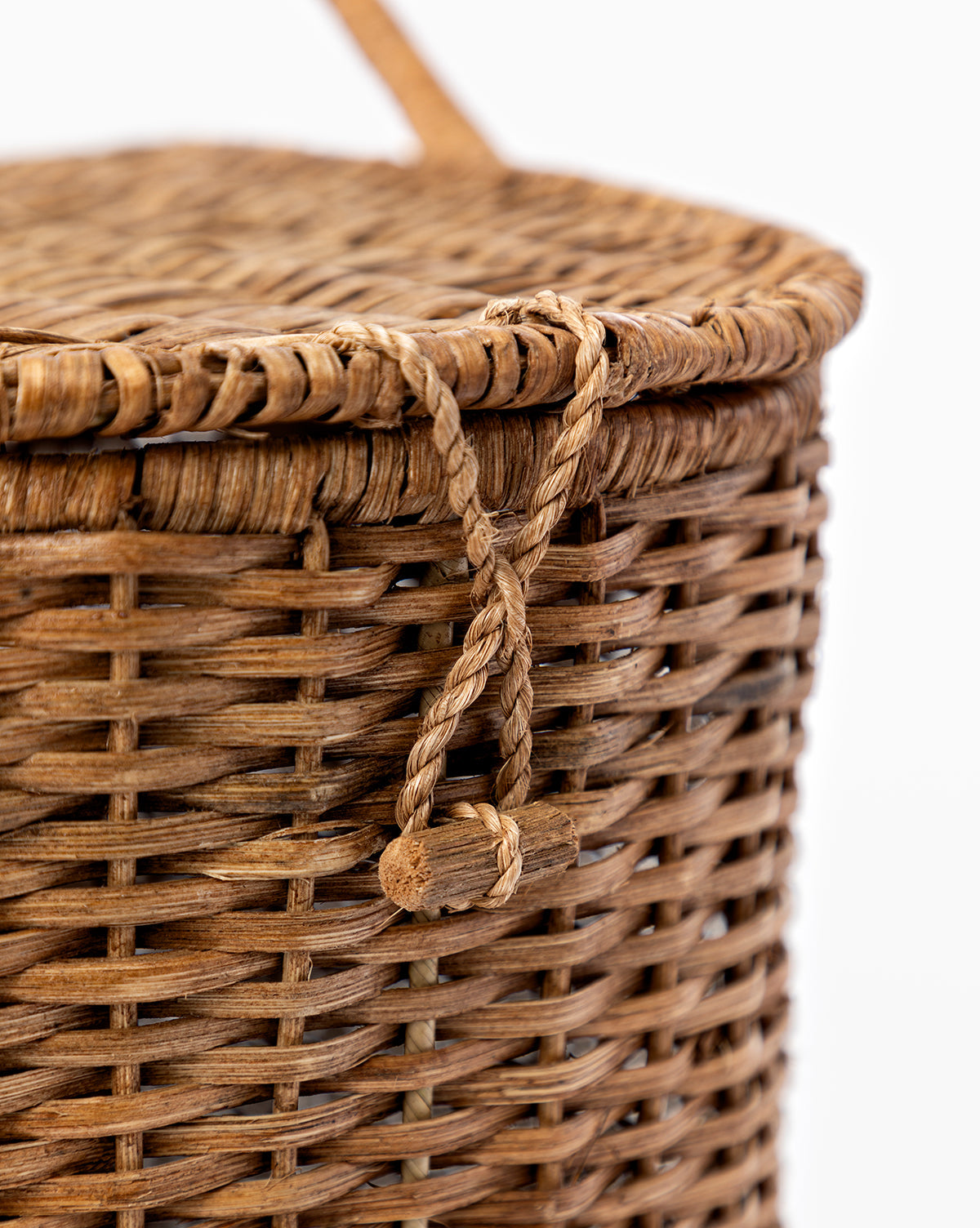 Close-up of the Rattan Wicker Picnic Basket featuring a braided loop and wooden toggle on its lid, this basket offers detailed texture and serves as a stylish storage solution for any room, by McGee & Co.