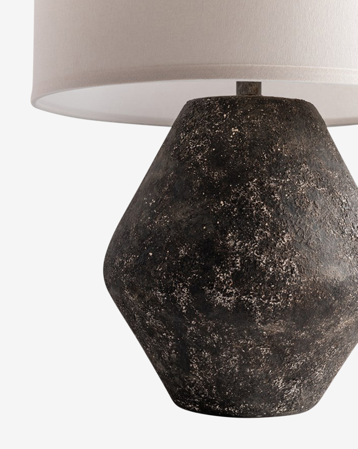 Close-up of the Rayan Table Lamp, showcasing its textured dark geometric stone base in a graystone finish paired with a white fabric drum shade against a plain, neutral background, by McGee & Co.