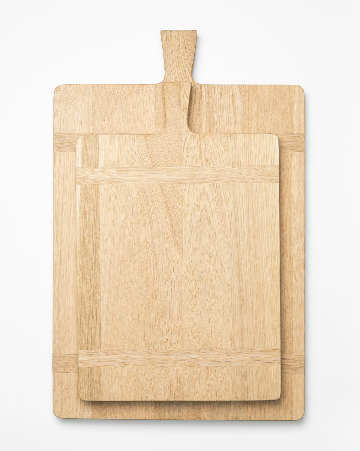 Two Rectangle Bread Boards with handles, made from oak and walnut, are stacked on a white surface. The smaller board sits on the larger, both showcasing their natural finish and unique wood grain, by McGee & Co.