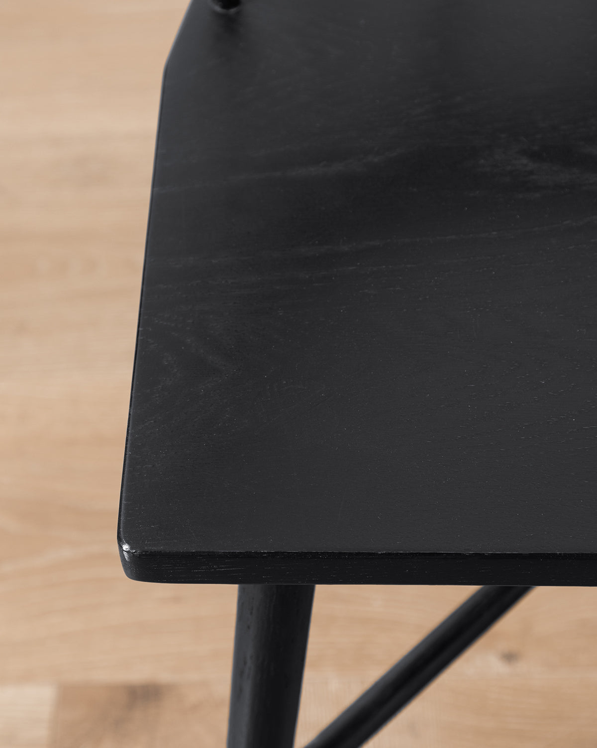 Close-up of a black wooden table corner with a smooth surface, positioned near the sleek Reeves Dining Chair on a light wood floor, highlighting the table’s edge and leg details, by McGee & Co.