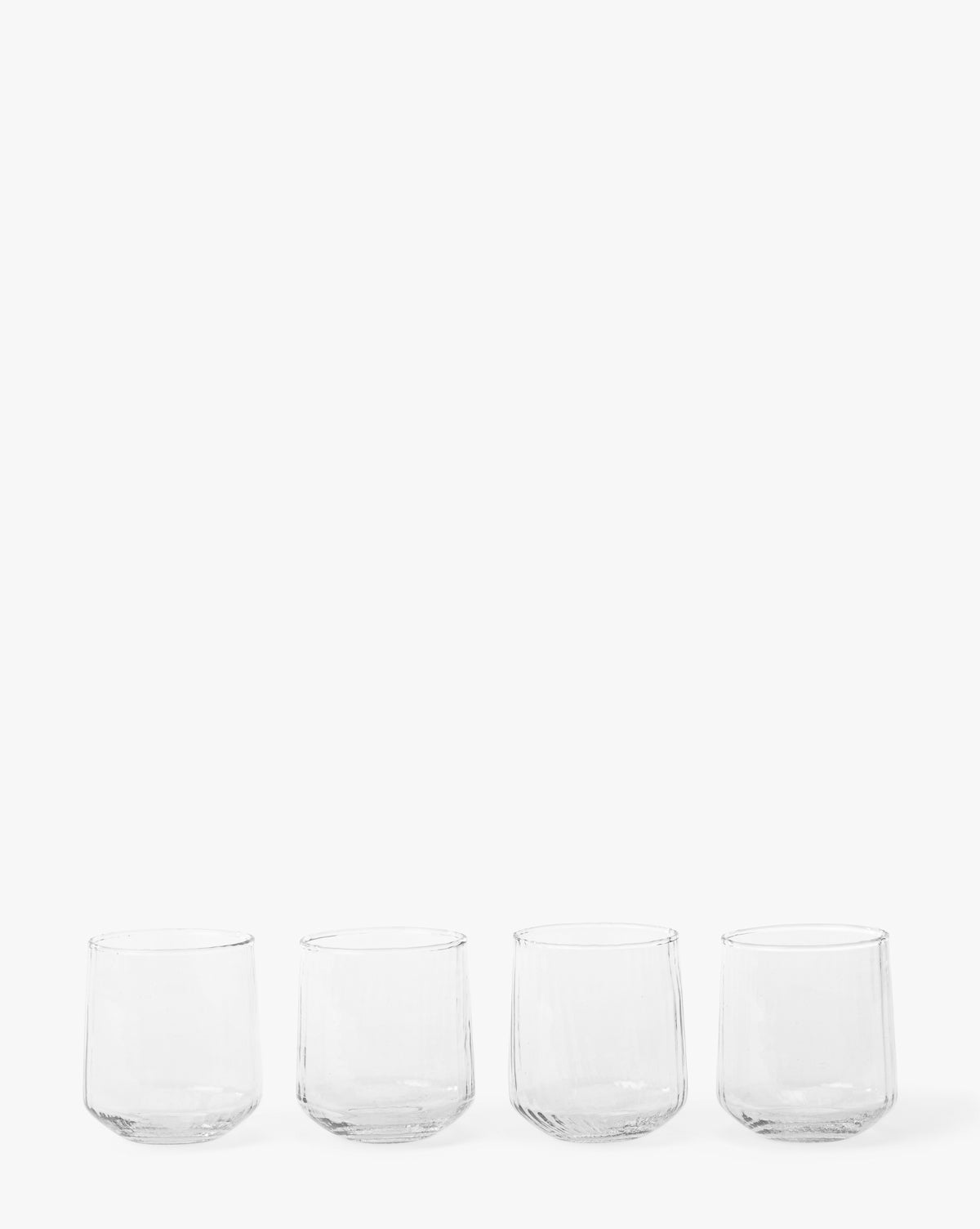 A set of four Ribbed Short Drinking Glasses is displayed in a row against a plain white background, by McGee & Co.